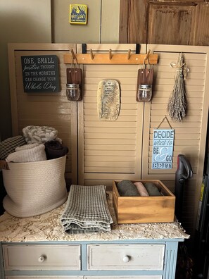 A cozy room with a wooden wall, a chalkboard with motivational quotes, a small shelf with jars, a basket of blankets, a box of towels, and a sign encouraging decision-making. - Charming loft cabin just 7 minutes from downtown (Talkeetna)