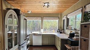 A kitchen with wooden ceiling, a refrigerator, cabinets, a sink, and a window with a view of trees. - Charming loft cabin just 7 minutes from downtown (Talkeetna)