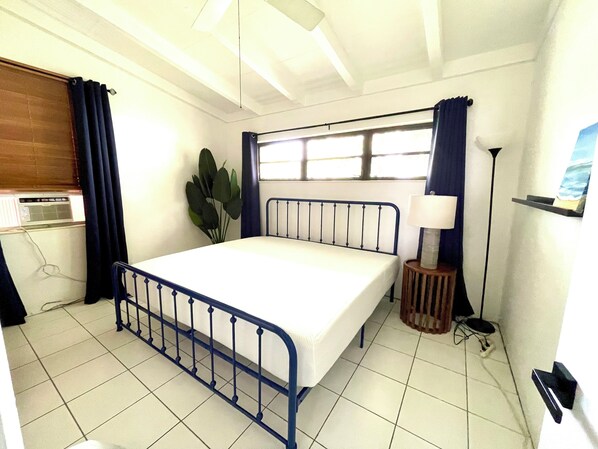 A bedroom with a bed, a window with curtains, a plant, a bedside lamp, and a radiator.