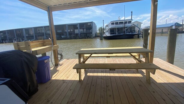 A wooden deck with a bench and picnic table, overlooking a marina with boats and buildings. - Blue crab house boat,Wi-Fi,Ice machine,sleeps 8,perfect place to fish🐠🎣🐟 (Venice)
