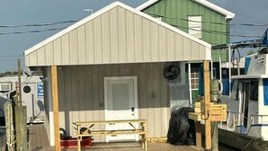 A floating structure with a wooden deck, a door, and a small table. - Blue crab house boat,Wi-Fi,Ice machine,sleeps 8,perfect place to fish🐠🎣🐟 (Venice)