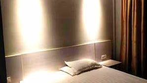 A hotel room with a bed, a nightstand, and a wall-mounted light fixture. - Xinsihai Hotel (Ningbo)