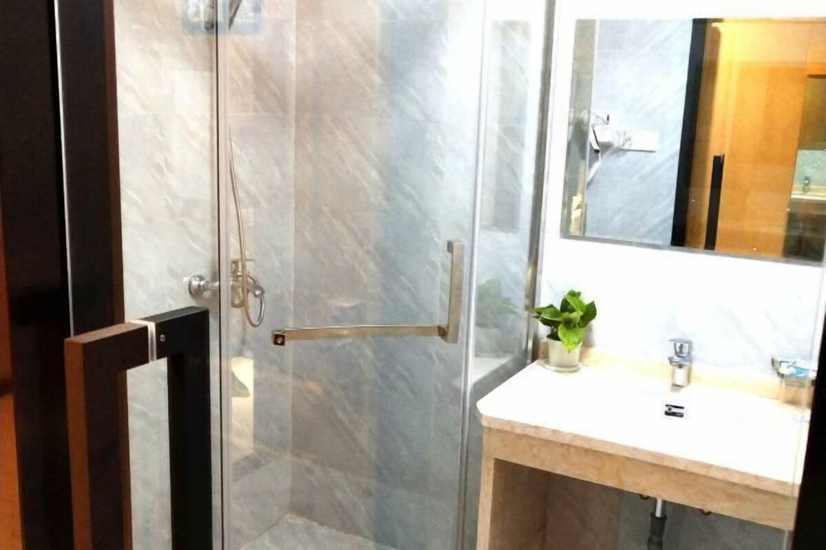 A bathroom with a glass shower door, a wooden vanity, a mirror, and a potted plant.