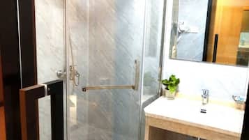 Un baño con mampara de vidrio, tocador de madera, espejo y planta en maceta.