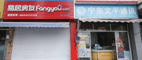 A storefront with a red sign, a closed shutter, and a blue awning.