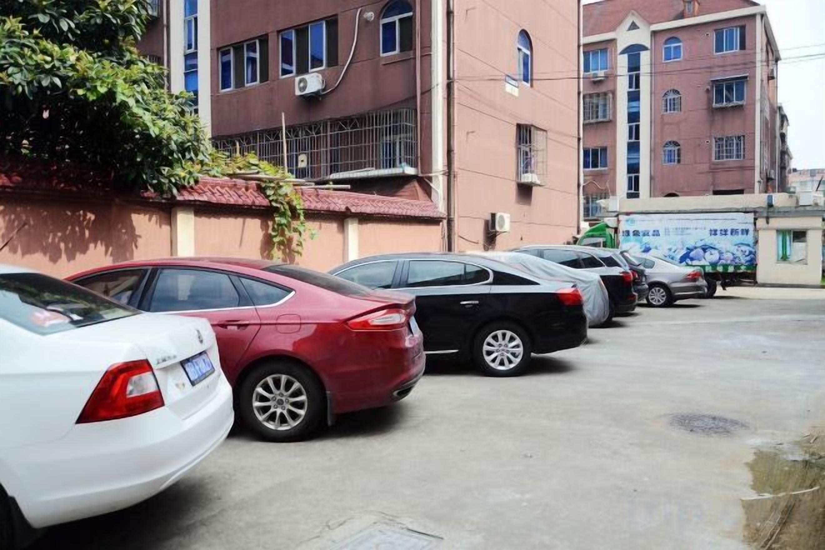 Un parking où sont garées plusieurs voitures devant un immeuble à étages, doté de nombreuses fenêtres.