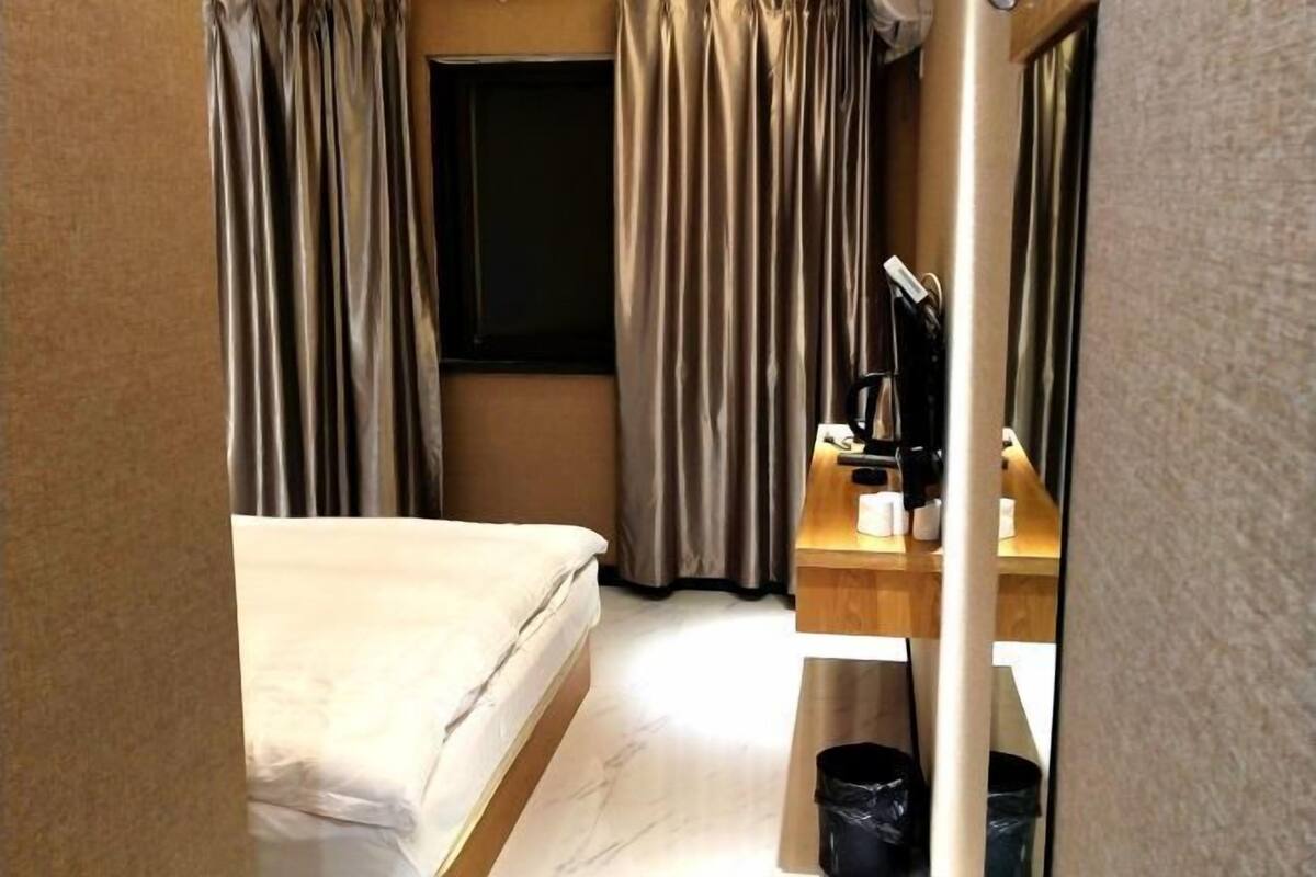 A hotel room with a bed, a desk with a computer, and a window.
