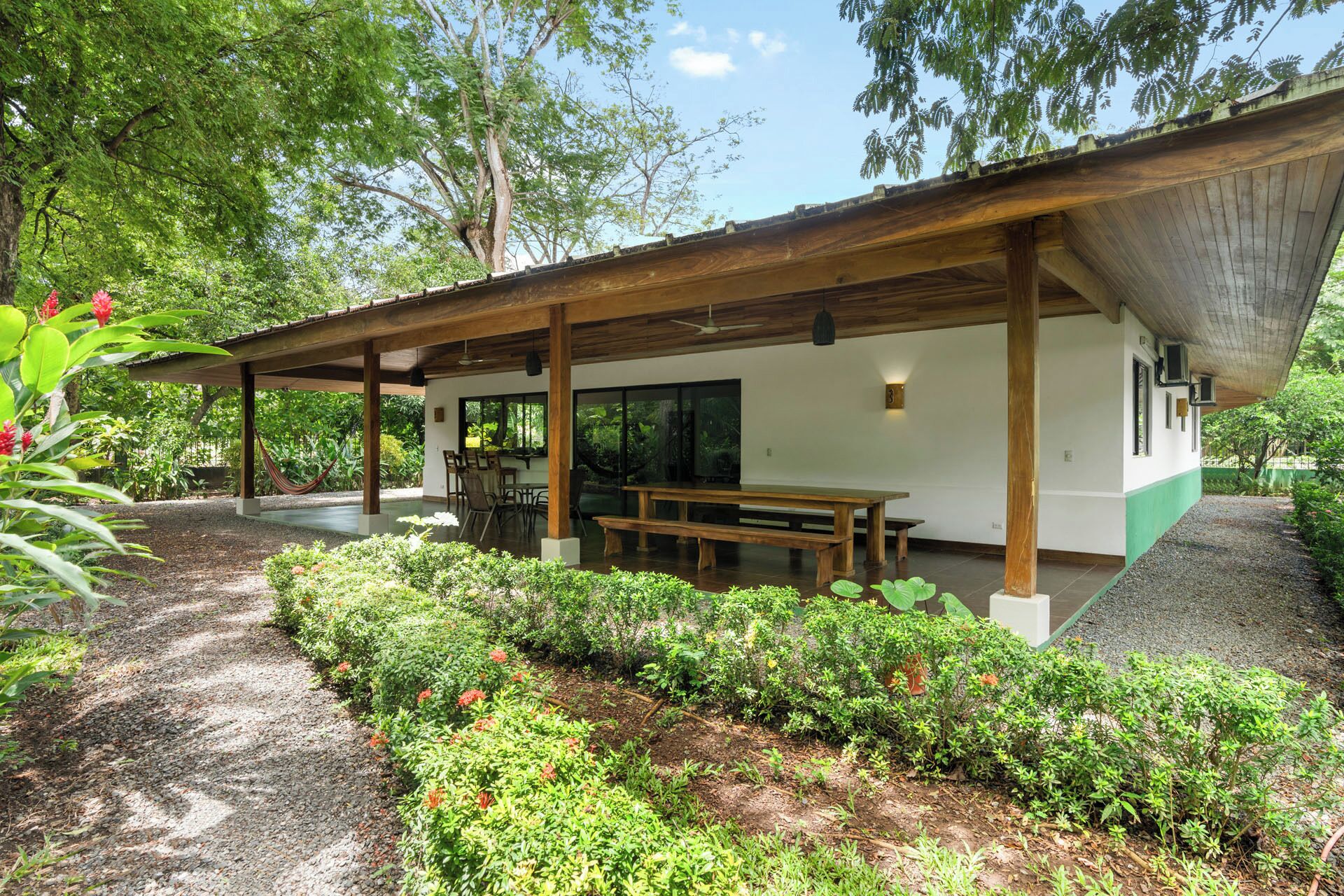 Un espace extérieur abrité comprenant un banc en bois, une table à manger et un hamac.