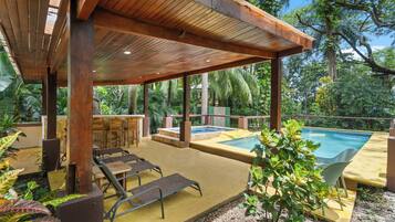 An outdoor pool area with a wooden deck, lounge chairs, and a bar.
