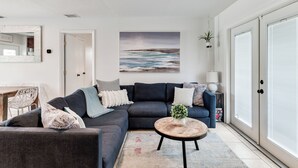 A modern living room with a dark grey sectional sofa, a round coffee table, and a large painting of a coastal scene. - Relax & Recharge: Saltwater Pool + Lush Backyard Oasis in Palm Beach Gardens (Palm Beach Gardens)