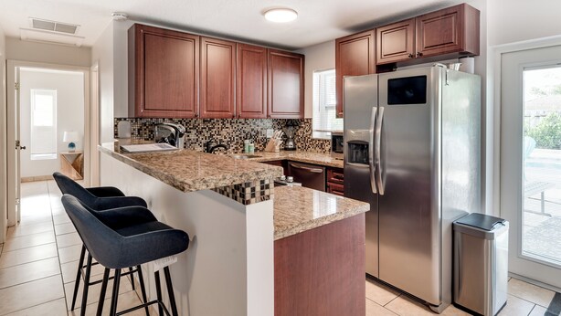 A kitchen with wooden cabinets, a stainless steel refrigerator, and a granite countertop. - Relax & Recharge: Saltwater Pool + Lush Backyard Oasis in Palm Beach Gardens (Palm Beach Gardens)