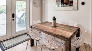 A dining area with a wooden table, white chairs, a decorative vase, a mirror, and a door with a view of the outside. - Relax & Recharge: Saltwater Pool + Lush Backyard Oasis in Palm Beach Gardens (Palm Beach Gardens)