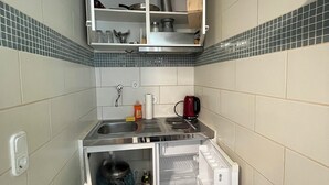 A compact kitchen with a built-in refrigerator, a sink, and a small countertop. - Cozy 1-room apartment (Hannover)