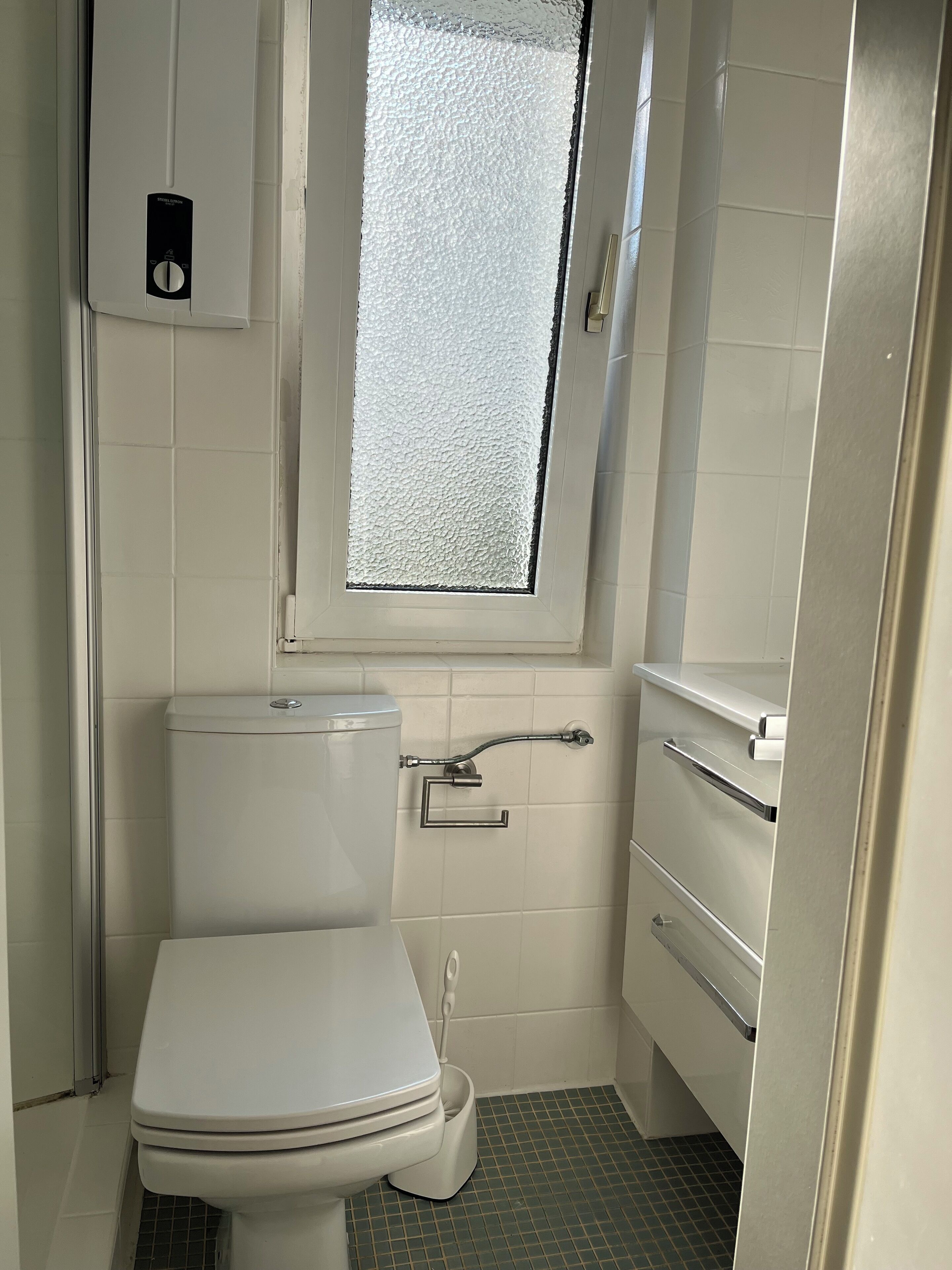 Ein kleines, kompaktes Badezimmer mit Toilette, Fenster und Waschbecken.