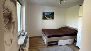 A bedroom with a bed, a radiator, a window, a painting, and a small desk with a chair. - Cozy 1-room apartment (Hannover)