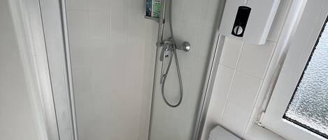 A small, modern bathroom with a glass-enclosed shower, a toilet, and a window.