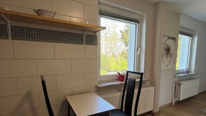 A kitchen with a dining table and chairs, a window with a view of greenery, and a radiator under the window. - Cozy 1-room apartment (Hannover)
