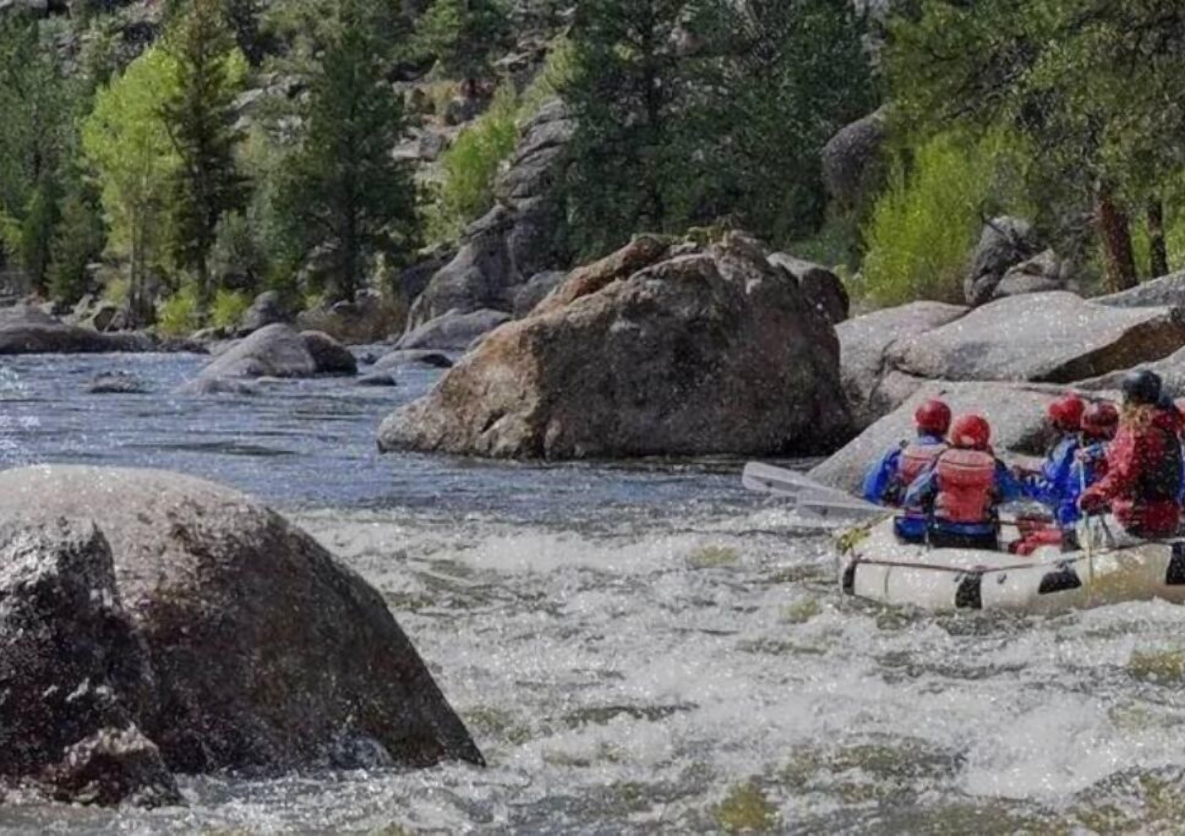 Een rivier met grote rotsen en een vlot waarop mensen helmen dragen.