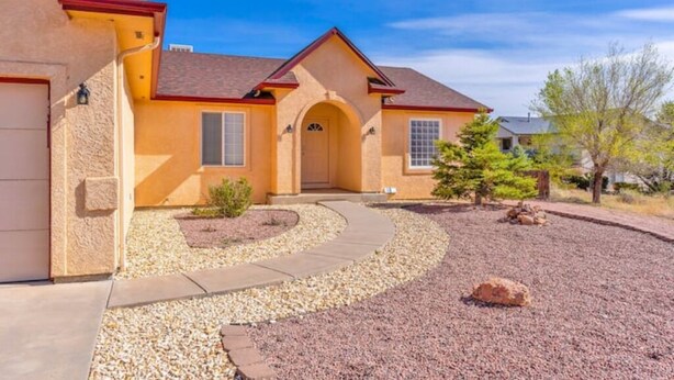 Una casa de un solo piso con fachada color beige, techo rojo y un camino curvo que lleva a la puerta principal.
