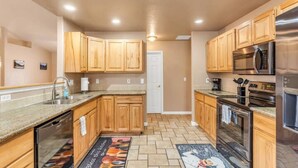 Una cocina con gabinetes de madera, electrodomésticos de acero inoxidable y piso de baldosas.
