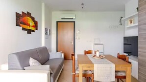 A modern living room with a grey sofa, a wooden dining table with chairs, a TV, and a wall-mounted artwork. - Fox's House - Apartment with private parking near Florence (Campi Bisenzio)