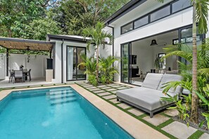 A modern house with a swimming pool, a patio with a table and chairs, and a large window overlooking the garden. - Modern Garden Villa with Private Pool, Outdoor Kitchen & Separate Casita Near Playa Potrero (Potrero)