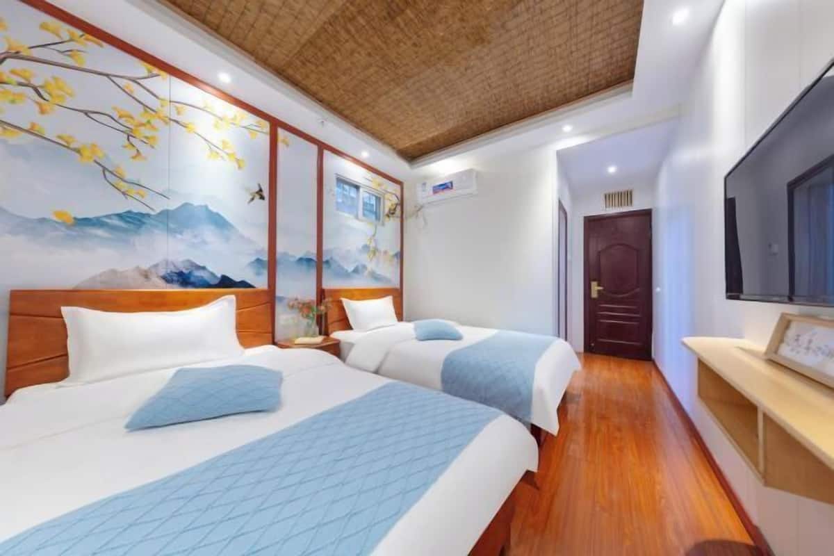 Une chambre d’hôtel avec deux lits, un plafond en bois, une fresque murale, un téléviseur et une porte.