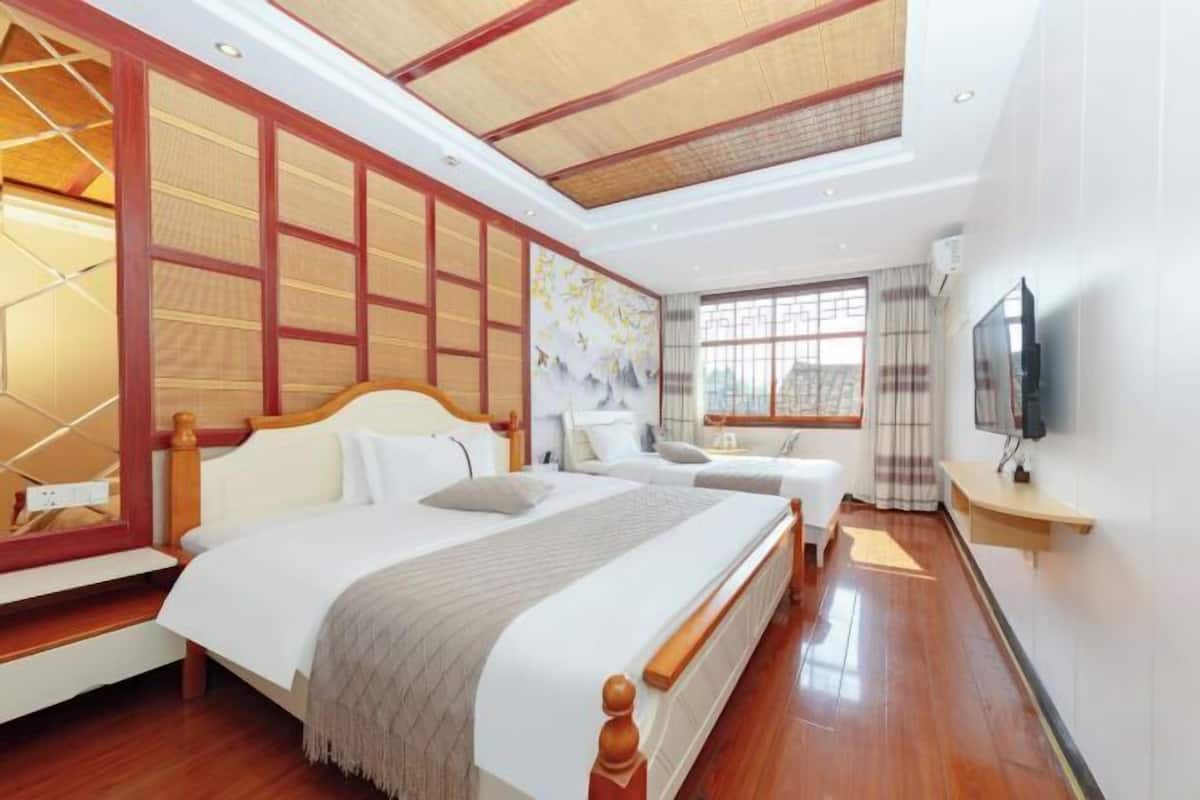 Une chambre d’hôtel avec un grand lit, une tête de lit en bois, une télévision et une fenêtre avec des rideaux.