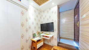 Una habitación con televisión sobre un mueble bajo, un escritorio pequeño con una silla y suelo de madera.