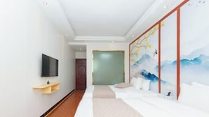 Una habitación de hotel moderna con suelo de madera, un televisor de pantalla plana montado en la pared, un sofá con cojines y un cuadro grande de montañas y pájaros.