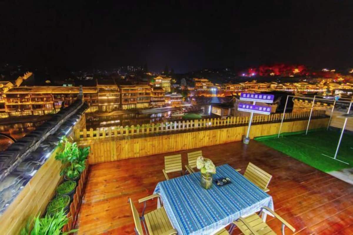 Une terrasse sur le toit, avec une table et des chaises, entourée d’une clôture en bois et agrémentée de plantes en pot.