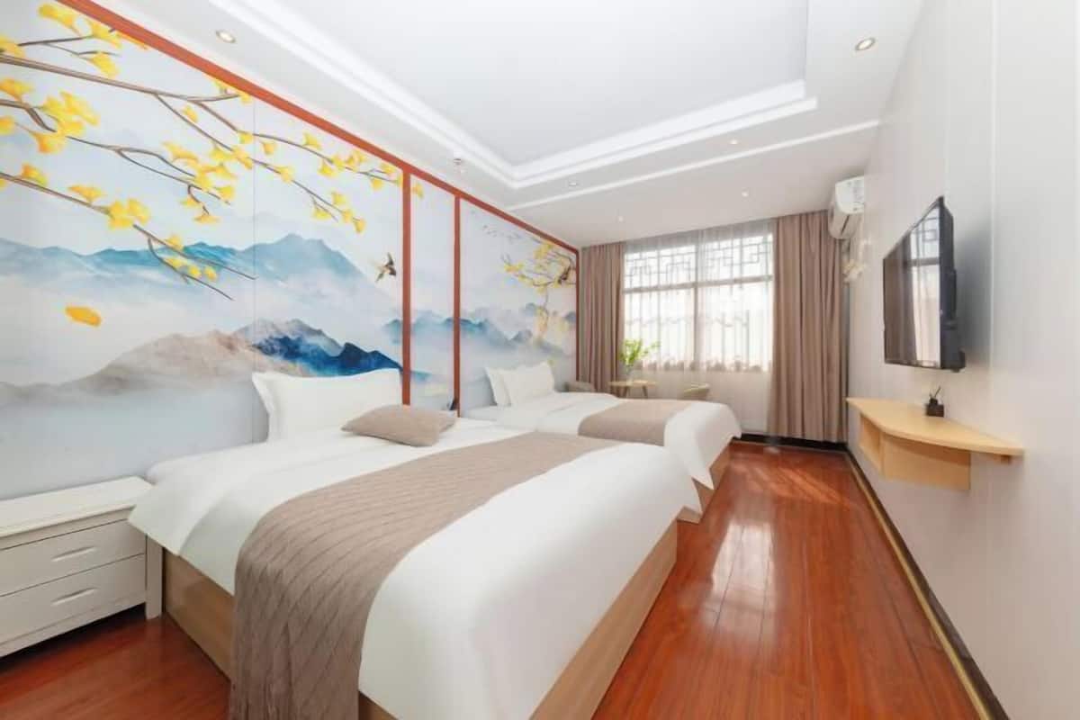 Une chambre d’hôtel avec deux lits, une grande fresque murale, un plancher en bois et un téléviseur fixé au mur.