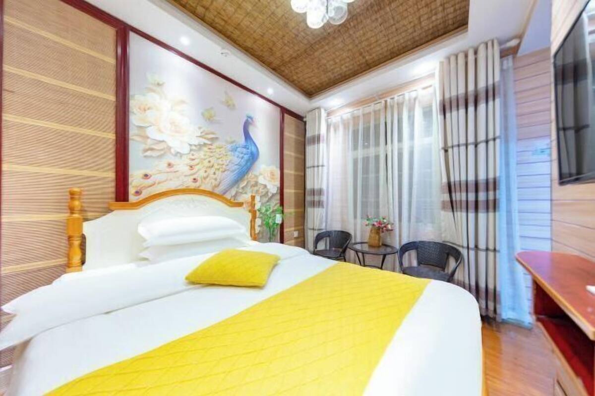 Une chambre d’hôtel avec un lit, une tête de lit en bois, une fresque murale, une fenêtre avec des rideaux et une petite table avec des chaises.