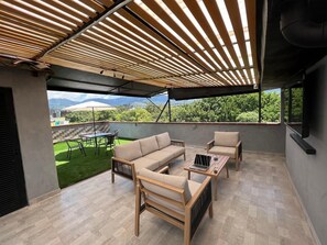 Un espacio al aire libre cubierto con sofás, sillas y una mesa, con vistas a un césped verde y edificios a lo lejos.