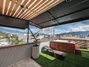 En balkon med træloft, en potteplante, en metalstol og en træbænk.