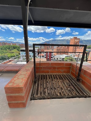 A rooftop terrace with a brick wall, a metal railing, and a view of buildings and mountains. - CAVE (Medellín)
