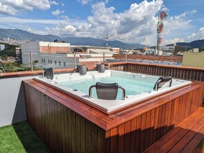 A rooftop pool with wooden deck, hot tub, and seating. - CAVE (Medellín)