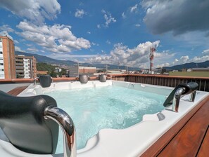 Un jacuzzi con asientos en una terraza, con vista a un paisaje urbano y montañas al fondo.