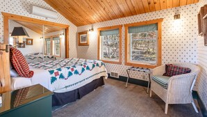 A cozy bedroom with a wooden ceiling, a bed with a quilt, two windows with checkered curtains, a wicker chair, and a mirror. - Sisters Chalet 1-bed retreat with WiFi, AC, and views near downtown Sisters. (Sisters)