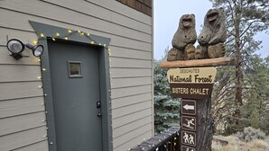 A wooden door with a keypad lock, a sign for Deschutes National Forest Sisters Chalet, and a wooden fence with lights. - Sisters Chalet 1-bed retreat with WiFi, AC, and views near downtown Sisters. (Sisters)