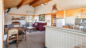 A cozy cabin interior with a dining area, a living room with a sofa, and a kitchen area with wooden cabinets and a refrigerator. - Sisters Chalet 1-bed retreat with WiFi, AC, and views near downtown Sisters. (Sisters)