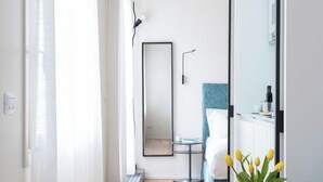 Una habitación de hotel moderna con piso de madera, una cama con cabecera azul, una mesita de noche, un espejo y una pequeña mesa redonda con un jarrón de flores.