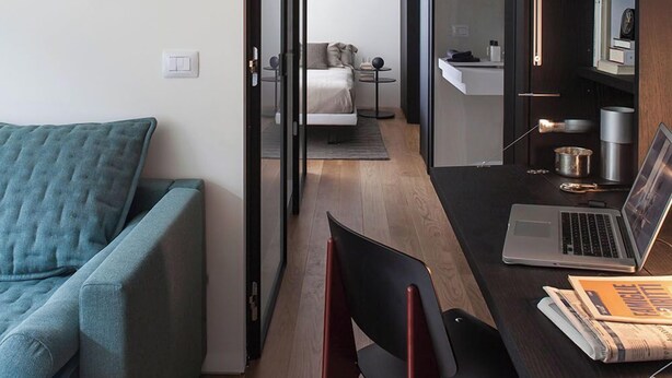 Un espacio habitable moderno y funcional, con un sofá, un escritorio con una computadora portátil y una estantería.
