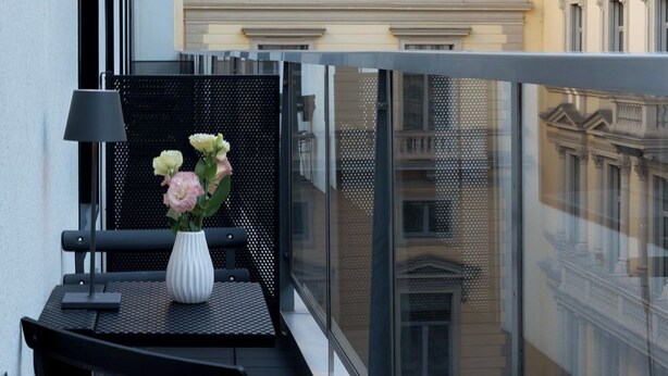 A balcony with a table and chairs, a vase with flowers, and a view of historic buildings.