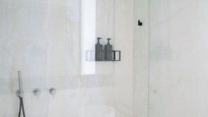 A modern bathroom with a glass shower enclosure, a handheld showerhead, and a wall-mounted faucet.