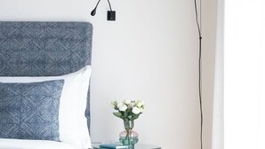 A bedroom with a bed, a bedside table with books, a vase with flowers, and a floor lamp. - Penthouse Apartment 5.4 (Milano)