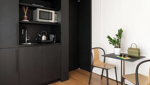 A compact kitchen with a microwave, kettle, and modern sink. A small table with chairs and a potted plant is visible. - Penthouse Apartment 5.4 (Milano)