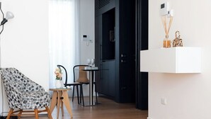 A modern living room with a patterned armchair, a small round table with a vase, a dining area with chairs, and a red sofa. - Penthouse apartment 5.BMORE (Milano)