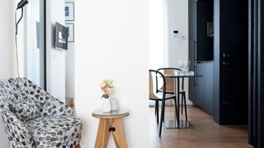 A modern living room with a patterned armchair, a small round table with a vase of flowers, and a dining area with chairs and a glass table. - Penthouse apartment 5.BMORE (Milano)