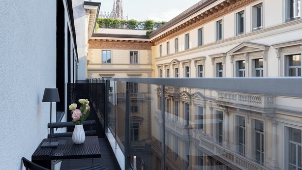 A balcony with a table and a vase of flowers, overlooking a cityscape with classical architecture. - Penthouse apartment 5.BMORE (Milano)